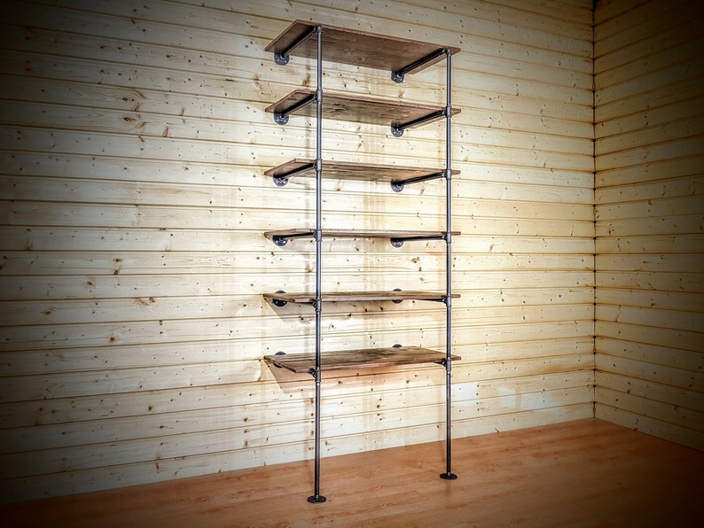 May include: A black metal pipe shelving unit with five wooden shelves. The shelves are made of reclaimed wood and have a rustic look. The unit is mounted to a wall and has a minimalist design.