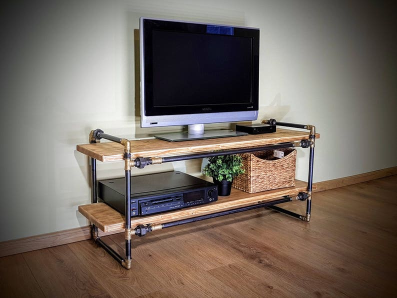 May include: A black metal TV stand with two wooden shelves and gold accents. The stand has a black TV on top, a black stereo system on the bottom shelf, and a wicker basket on the top shelf.