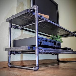 May include: A black metal TV stand with two shelves. The stand is made of industrial pipes and has a rustic wood top. A black stereo system is on the bottom shelf.