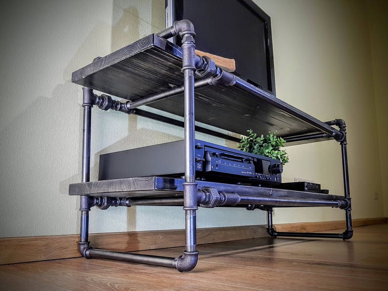 May include: A black metal TV stand with two shelves. The stand is made of industrial pipes and has a rustic wood top. A black stereo system is on the bottom shelf.