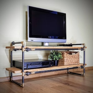May include: A black metal TV stand with two shelves, a wood top, and a black TV on top. The stand has a plant and a wicker basket on the bottom shelf.
