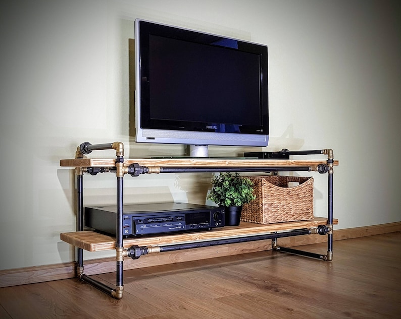 May include: A black metal TV stand with two shelves, a wood top, and a black TV on top. The stand has a plant and a wicker basket on the bottom shelf.