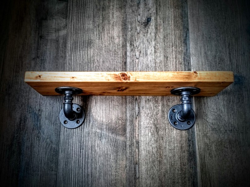 May include: A wooden shelf with black metal pipe brackets. The shelf is mounted on a wood wall.