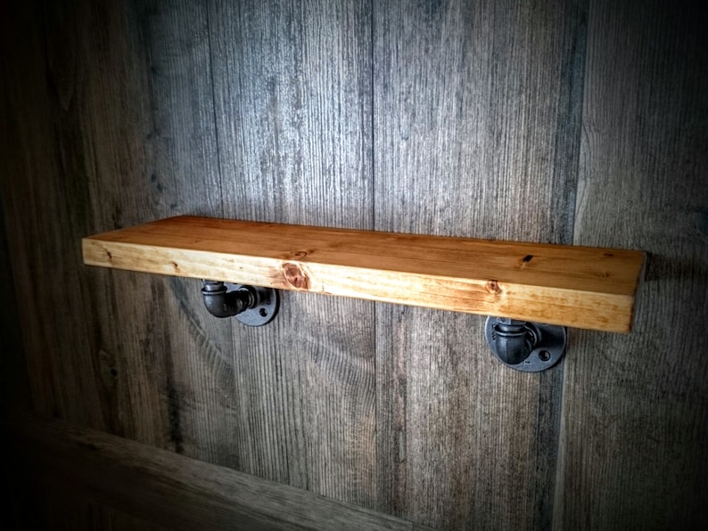 May include: A wooden shelf with black metal pipe brackets. The shelf is mounted on a wood wall.