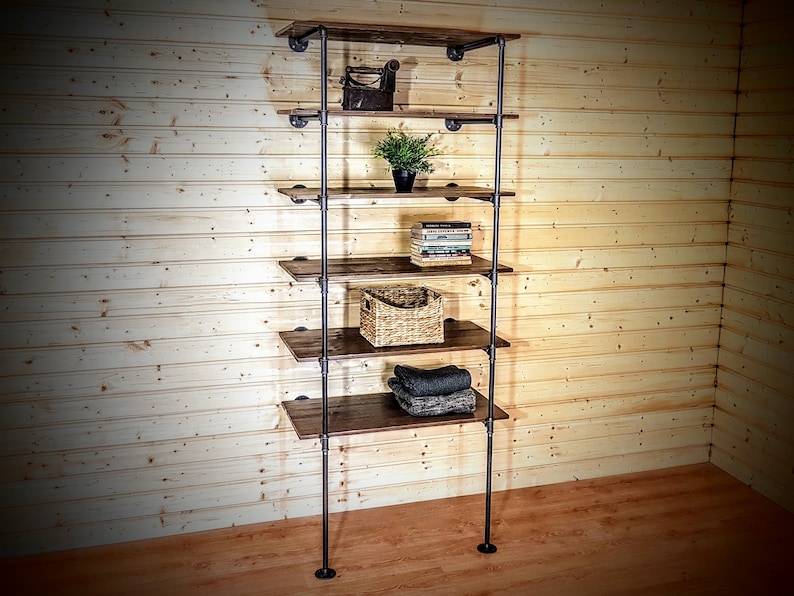 May include: A six-shelf industrial pipe and wood shelf unit with a rustic brown finish. The shelves are filled with various items, including a small iron object, a potted plant, books, a wicker basket, and folded fabric.