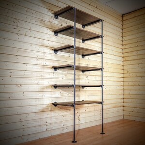 May include: A tall, industrial-style shelving unit with five wooden shelves and black metal pipes. The shelves are made of dark wood and are supported by black metal pipes. The unit is freestanding and is shown against a wood-paneled wall.