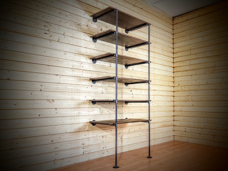 May include: A tall, industrial-style shelving unit with five wooden shelves and black metal pipes. The shelves are made of dark wood and are supported by black metal pipes. The unit is freestanding and is shown against a wood-paneled wall.