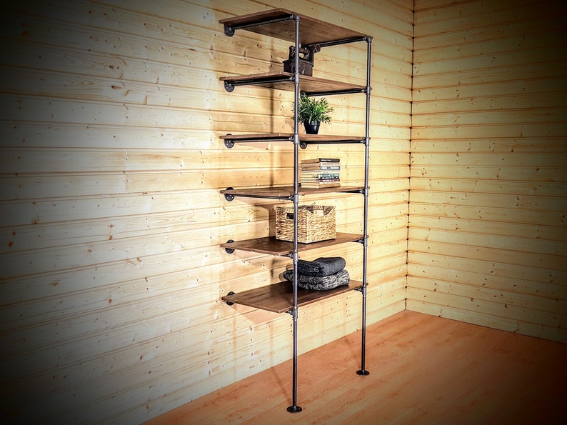 May include: A six-shelf industrial pipe shelving unit with wooden shelves. The shelves are filled with various items, including a potted plant, books, a woven basket, and folded towels.