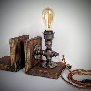 May include: A rustic wooden bookend lamp with a black metal pipe base and a vintage Edison bulb. The lamp has a brown cord and a black plug.
