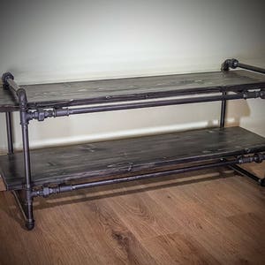 May include: A two-tiered shelf made of black metal pipes and dark wood planks. The shelf is sturdy and has a rustic industrial style.