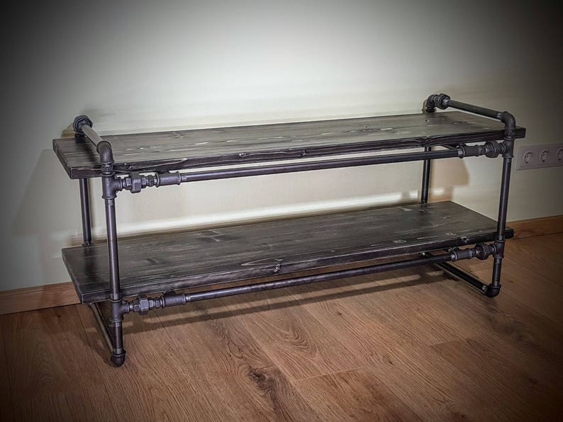 May include: A two-tiered shelf made of black metal pipes and dark wood planks. The shelf is sturdy and has a rustic industrial style.