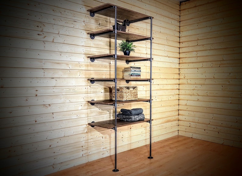 May include: A black metal pipe shelving unit with five wooden shelves. The shelves are filled with various items, including a potted plant, books, a wicker basket, and folded towels.