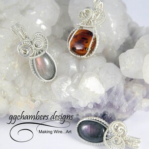 May include: Three silver wire wrapped pendants with different colored gemstones. The pendants are displayed on a white and purple background. The text "ggchambers designs Making Wire...Art" is visible in the bottom left corner of the image.