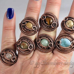 Puede incluir: Un maniquí de mano con siete anillos de alambre de cobre envueltos con piedras preciosas de diferentes colores. Los anillos presentan un diseño único con un alambre circular envuelto alrededor de la piedra preciosa.