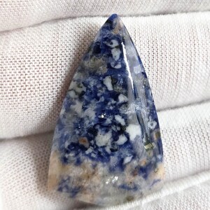 May include: A polished, triangular gemstone with a mix of deep blue, white, and tan colors. The stone has a smooth, glossy surface and a unique pattern, likely a sodalite specimen.