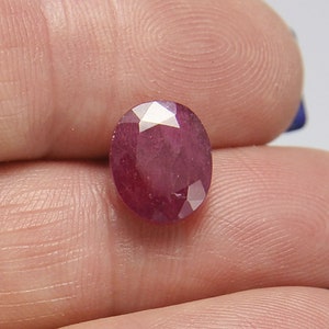 May include: A deep red oval-shaped gemstone with a faceted cut.