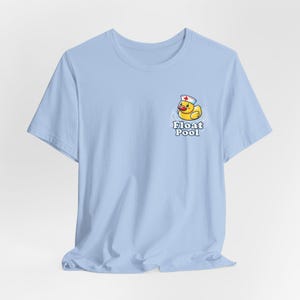 May include: Light blue t-shirt featuring a cartoon duck wearing a nurse's hat, with the text "Float Pool" below. The duck is yellow with a red beak and is surrounded by water ripples. The shirt is made of a soft material.
