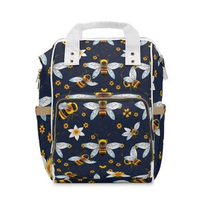 May include: A navy blue backpack with a white trim and a pattern of yellow and black bees on a white flower background.