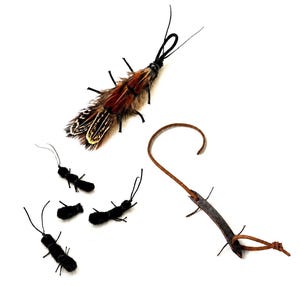 May include: A collection of insect-shaped toys including one large brown and black feathered insect with antennae, four small black fuzzy insect figures with thin antennae, and one brown leather strip shaped like a curved insect with legs.
