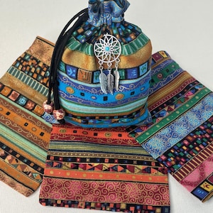 May include: A drawstring pouch made of multi-colored fabric featuring horizontal bands of geometric patterns in orange, blue, green, and gold. A silver-toned dreamcatcher charm with a small turquoise bead hangs from the black drawstring cords.