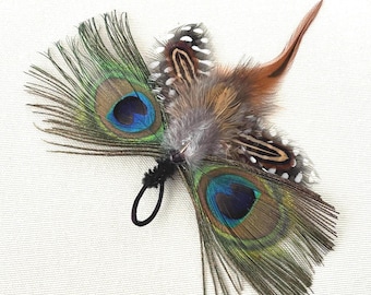 May include: A decorative hair accessory featuring peacock feathers with vibrant blue, green, and brown hues. The accessory includes a black elastic loop for attachment. Additional feathers in shades of brown, gray, and white are also included.