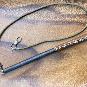 May include: A brown leather-wrapped metal stick with white stitching. The stick is attached to a green cord with a silver key ring.