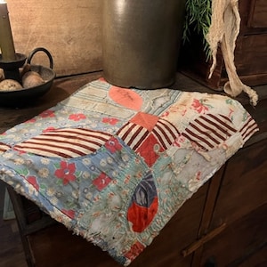 May include: A patchwork quilt with a variety of floral and striped patterns in shades of red, blue, and white. The quilt is made of different fabrics and has a rustic, vintage look.