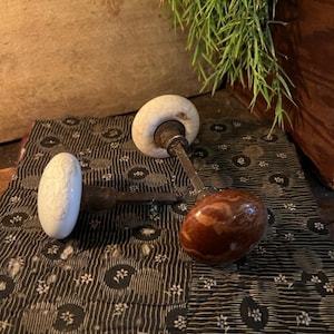 May include: Two antique porcelain door knobs with brown and white painted designs. The knobs are on a black and white fabric with a floral pattern.