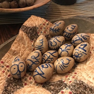 May include: A collection of 12 decorative eggs, painted in a rustic style with blue and white designs. The eggs are displayed in a wooden bowl lined with a fabric napkin.