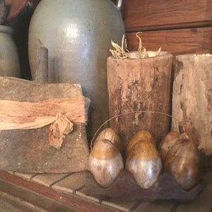 May include: A collection of rustic home decor items, including a wooden axe, two wooden cylinders, and a group of six brown and white eggs. The items are arranged on a wooden shelf with a brown and white striped fabric.