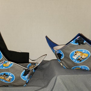 Può includere: Due scaldavivande in tessuto grigio con un motivo blu e bianco con personaggi dei cartoni animati di Star Wars. Gli scaldavivande sono piegati e mostrati su una superficie grigia.