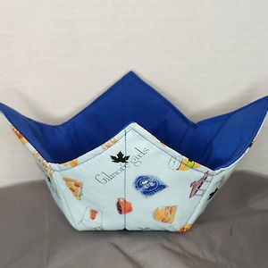 May include: A blue and white fabric bowl with a Gilmore Girls theme. The bowl is lined with blue fabric and features a pattern of food and drinks from the show.