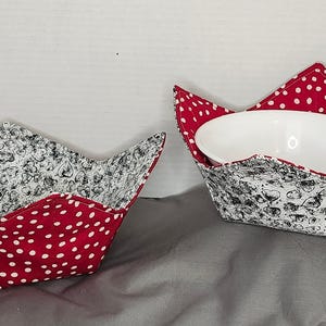 May include: Two red and white polka dot fabric bowl cosies. The larger cosy has a white bowl inside. Both cozies have a black and white floral pattern on the inside.