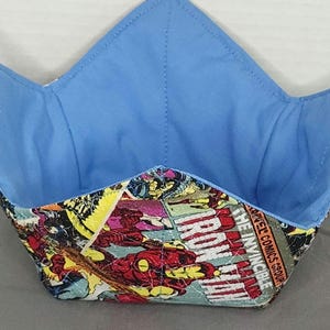 Puede incluir: Un protector de cuenco hecho a mano con un estampado de cómic con gráficos de Iron Man. El interior es azul claro y el exterior muestra paneles de cómic coloridos. El protector de cuenco está diseñado para mantener la comida caliente.