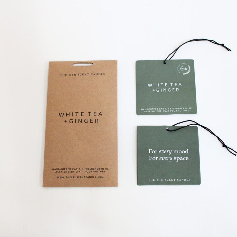 Puede incluir: Un conjunto de tres ambientadores de coche con un embalaje de papel marr&oacute;n y dos ambientadores verdes. Los ambientadores est&aacute;n hechos a mano y tienen el aroma de t&eacute; blanco y jengibre. El texto en el embalaje dice "The 8th Scent Candle" y "White Tea + Ginger". El texto en los ambientadores verdes dice "White Tea + Ginger", "Para cada estado de &aacute;nimo", "Para cada espacio" y "The 8th Scent Candle".