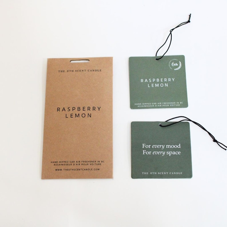 Puede incluir: Dos ambientadores de coche verdes con colgadores de cuerda negra. El de arriba dice "Raspberry Lemon" y el de abajo dice "For every mood, For every space". Ambos tienen el texto "The 6th Scent Candle" en ellos.