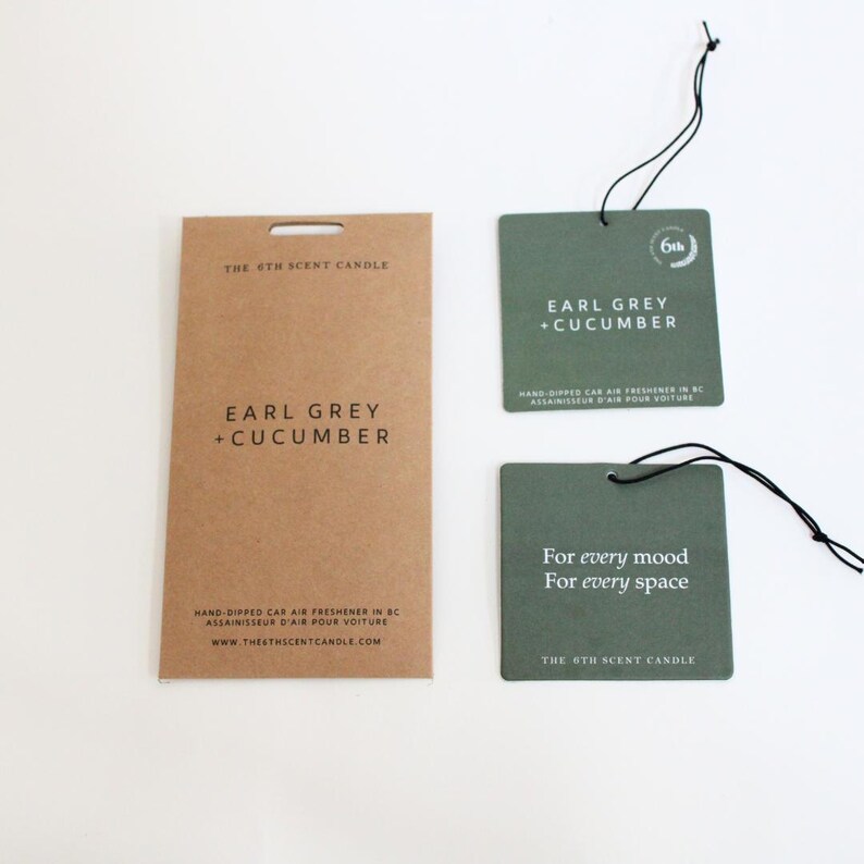 Puede incluir: Tres ambientadores de coche de color marr&oacute;n y verde con el texto "The 6th Scent Candle" y "Earl Grey + Cucumber".