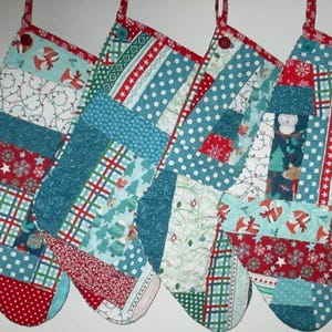 May include: Four handmade Christmas stockings with patchwork designs. Each stocking features a unique combination of red, teal, and white fabrics with patterns like polka dots, snowflakes, and Christmas trees. They have red hanging loops.