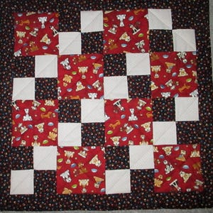 May include: A handmade quilt with a checkerboard pattern. Alternating squares of red fabric with dog-themed prints and white squares. The quilt is bordered with a black fabric featuring small, scattered paw prints and dots. A cozy, handcrafted item.