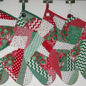May include: Five Christmas stockings hanging in a row, each crafted from a patchwork of various fabrics in red, green, and white. The patterns include polka dots, chevron stripes, and circular motifs, with a single button accent at the top of each.