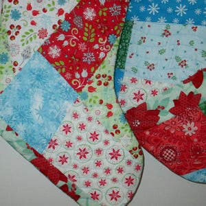 May include: Two Christmas stockings with patchwork patterns. One stocking features red, white, and blue snowflake and floral designs. The other stocking has red, green, and white floral patterns. Both are quilted.