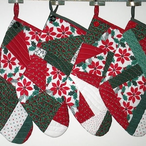 May include: Four quilted Christmas stockings featuring a patchwork design of red and white poinsettia floral fabric, dark green fabric with small patterns, and white fabric with red dots. Each stocking has a hanging loop and a single button at the top.