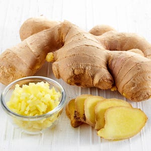 May include: A close-up shot of fresh ginger root, sliced ginger, and diced ginger in a glass bowl. The ginger root is a light brown color, and the sliced and diced ginger is a pale yellow. The image is set against a white background.