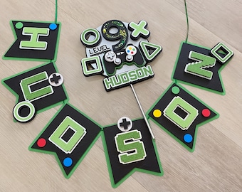 May include: A green and black banner with the letters "HUDSON" and the numbers "9" and "5" in a pixelated font. The banner is decorated with green and black game controller symbols and the words "LEVEL" and "HUDSON".