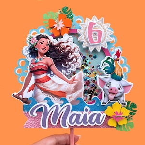 Puede incluir: Adorno de pastel colorido con una ilustraci&oacute;n de dibujos animados de una mujer polinesia, un cerdo y un gallo. El adorno incluye el nombre "Maia" y el n&uacute;mero "6". Presenta flores, hojas y lentejuelas sobre un fondo naranja.
