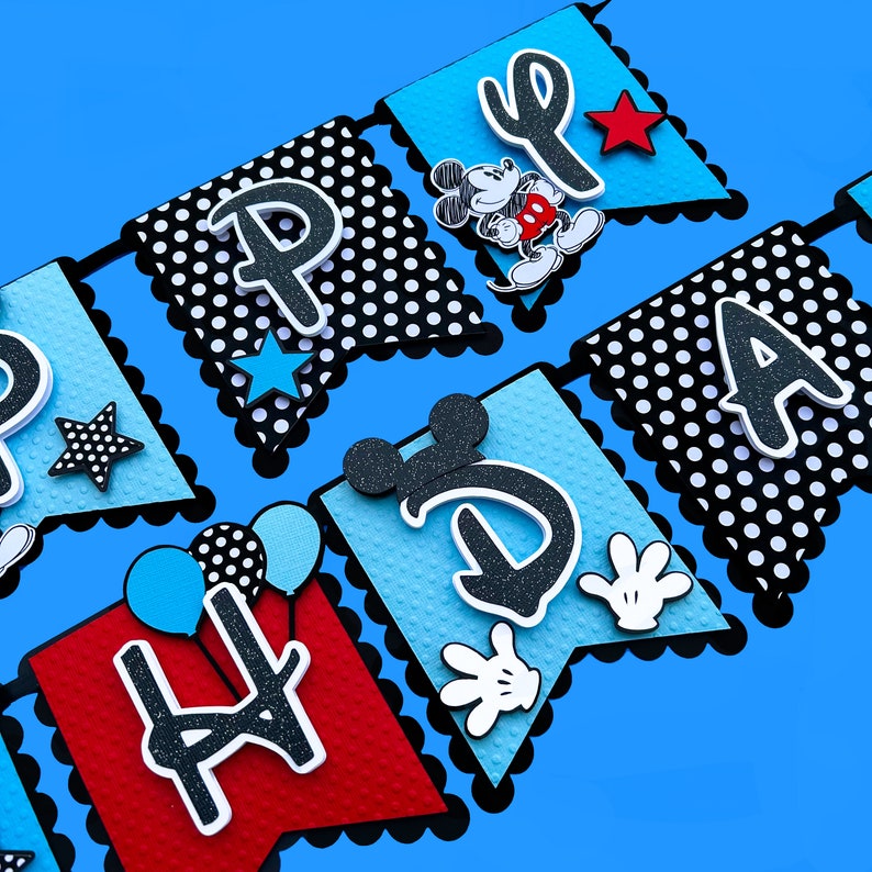 May include: Happy Birthday banner with black and white polka dots, blue and red flags, and Mickey Mouse characters. The banner spells out "Happy Birthday".