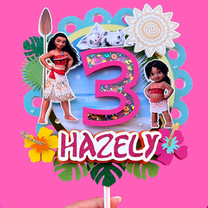 Puede incluir: Un vibrante adorno para pastel con el nombre "HAZELY" y el n&uacute;mero "3" con un elemento agitador. El dise&ntilde;o incluye ilustraciones de personajes de la pel&iacute;cula Moana, junto con flores tropicales y un sol. El fondo es rosa brillante.