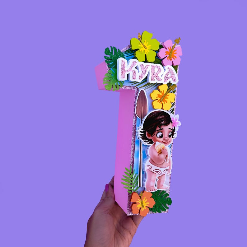 Puede incluir: Decoraci&oacute;n de cumplea&ntilde;os rosa con el n&uacute;mero uno y el nombre "Kyra" en letras blancas. La decoraci&oacute;n presenta una imagen de dibujos animados de una ni&ntilde;a, flores tropicales y una lanza. El fondo es azul claro con detalles brillantes.