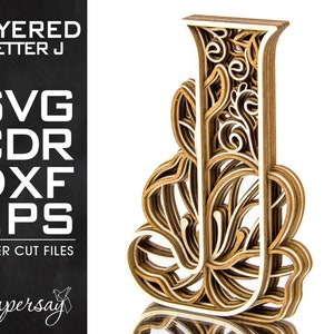 May include: Layered wooden letter J with intricate floral designs. The letter is made of multiple layers of wood, creating a 3D effect. The letter is a light brown color and has a white background.