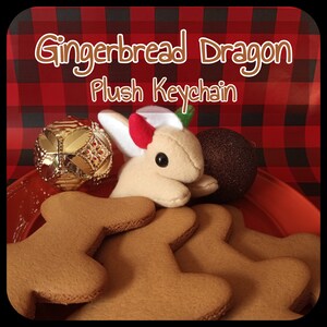 May include: Gingerbread Dragon Plush Keychain, a plush toy shaped like a gingerbread dragon with red horns, white fur, and brown eyes. The plush toy is sitting on top of gingerbread cookies.